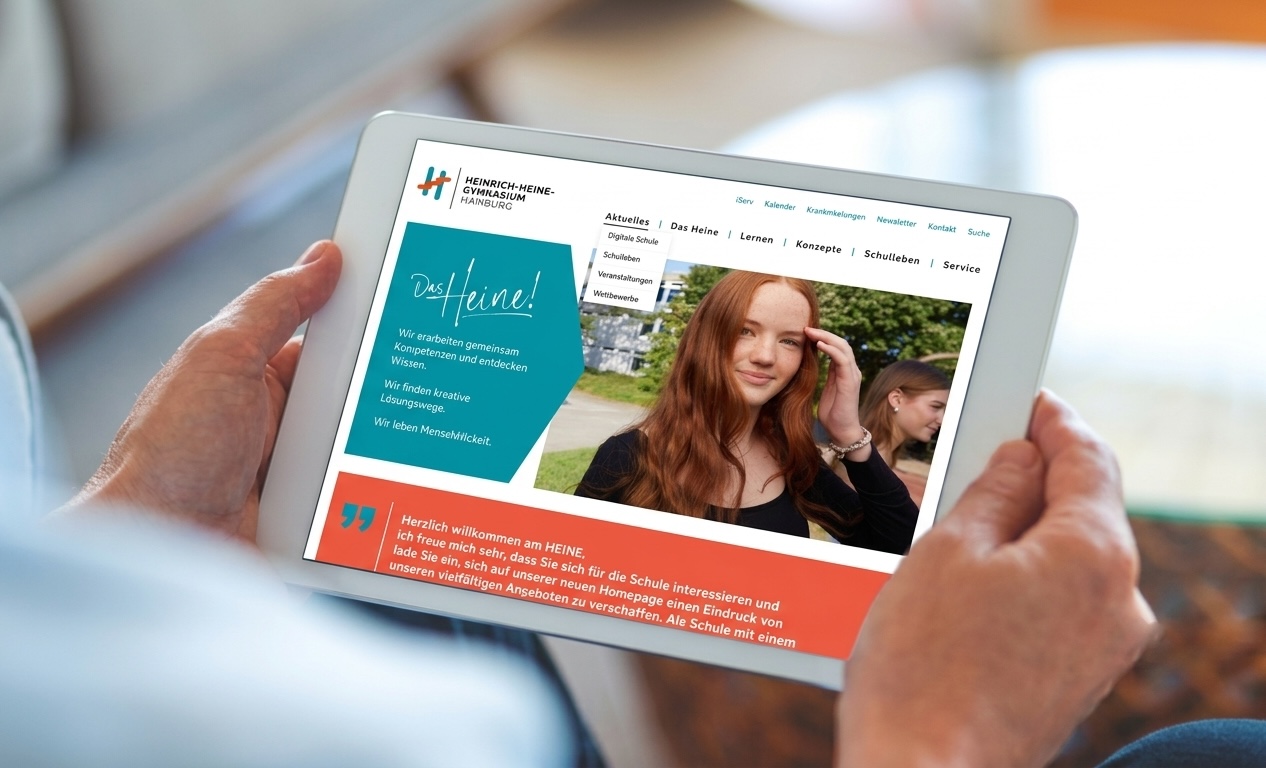 Eine Person, die ein Tablet in der Hand hält, zeigt eine Website mit dem Foto eines lächelnden Teenager-Mädchens und Informationen auf Deutsch über das Heinrich-Heine-Gymnasium. Die Website enthält Rubriken wie „Aktuelles“ und „Service“.